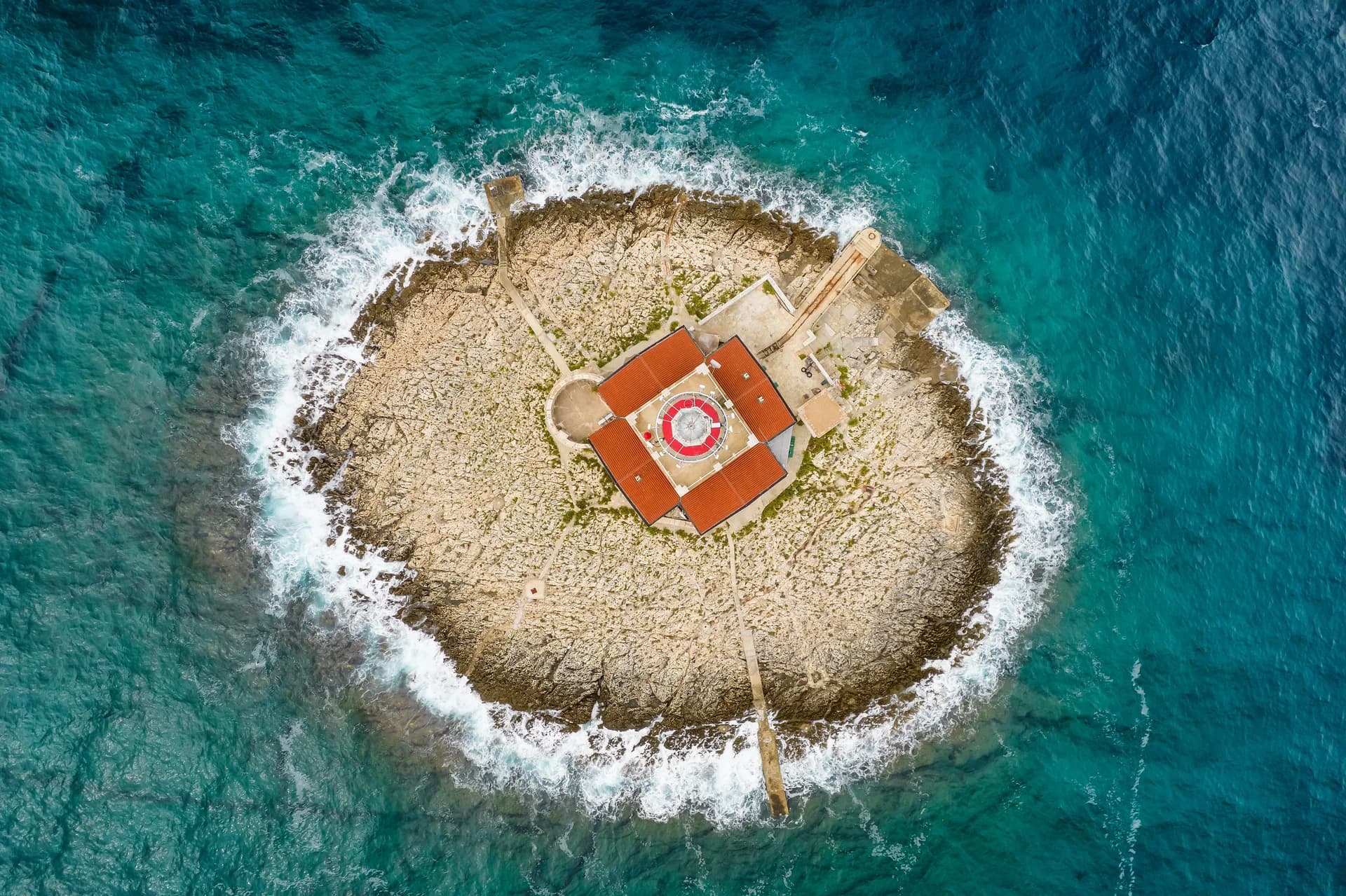 A lighthouse on a small rocky island, seen directly from above.